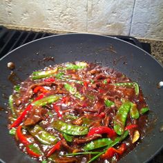 a wok filled with meat and vegetables on top of a grilling pan next to a stone wall