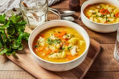 two bowls of soup are sitting on a cutting board next to a glass of water