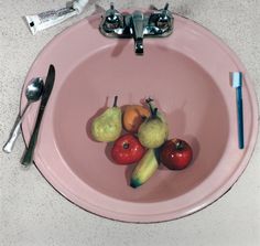 a pink bowl filled with fruit on top of a counter next to a knife and fork