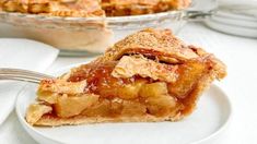 a slice of apple pie on a plate with a fork and bowl in the background