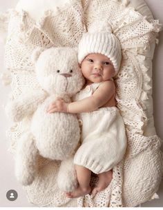 a baby laying next to a white teddy bear on top of a crocheted blanket