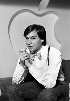 a man sitting on top of a couch in front of an apple logo wearing a bow tie