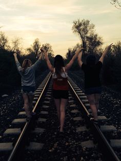 three girls walking on train tracks with their arms in the air