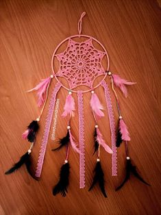 a pink dream catcher with black feathers on a wooden table next to a cell phone