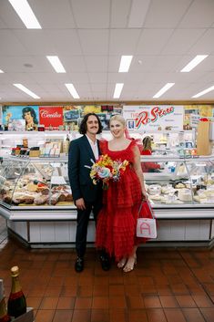 a man and woman standing in front of a display case at a deli filled with food