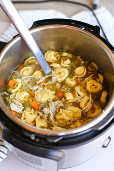 a pot filled with pasta and meat soup on top of a stove next to a silver spoon