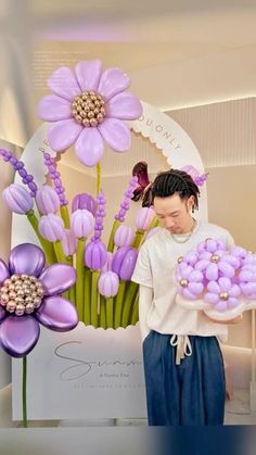 a woman is holding some balloons in front of purple flowers and orchids on display