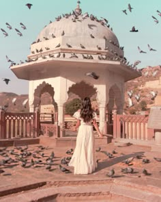 a woman standing in front of a white building with birds flying around her and on the ground