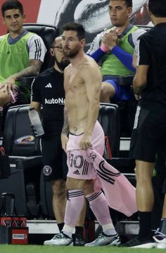 a shirtless man walking on the sidelines at a soccer game with other players behind him