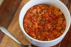 a white bowl filled with chili and rice on top of a wooden cutting board next to a spoon