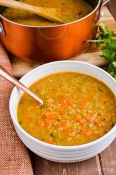 a bowl of soup with carrots and celery on the side next to a pot