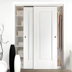 a white closet with two doors open next to a vase and black vase on the floor