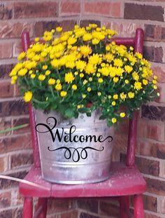 a metal bucket filled with yellow flowers sitting on top of a red chair next to a brick wall