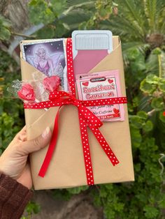 someone is holding up a wrapped gift in front of some plants and trees with flowers on it