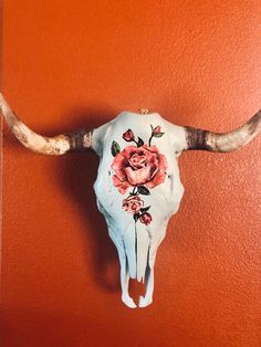 a cow skull with flowers painted on it's side hanging on a wall in an orange room