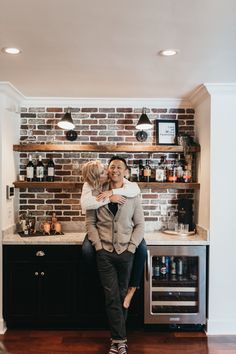 a man and woman hug in front of a brick wall with shelves on the other side