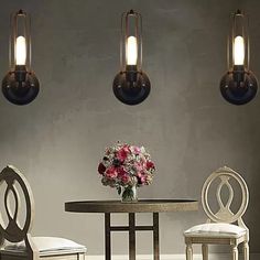 a dining room table and chairs with flowers on the table in front of two hanging lights