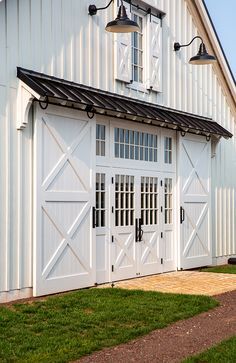 a white barn with an open door and two lights on the side of the building