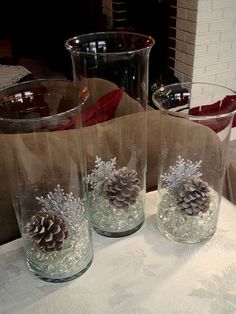 three glass vases with pine cones in them