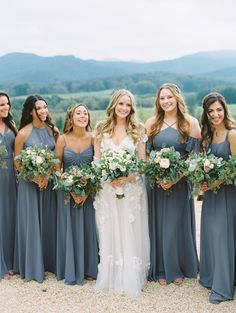 a group of women standing next to each other holding bouquets in front of mountains