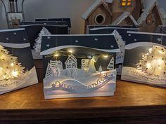 three christmas cards with lit up trees and houses in the background on a wooden table