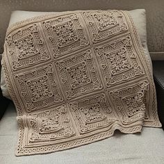 a white crocheted blanket sitting on top of a couch next to a pillow