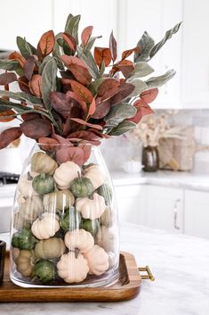 a glass vase filled with green and white pumpkins on top of a wooden tray