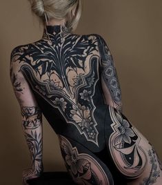 the back of a woman's body with tattoos on her chest and legs, sitting in front of a brown background