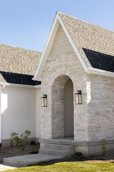 a white brick house with a black roof and two lights on the front door is shown