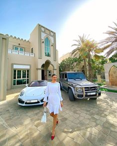 a woman is standing in front of two mercedes benzs and a luxury car on the driveway