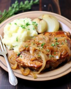 a plate with meat, onions and mashed potatoes on it next to a fork