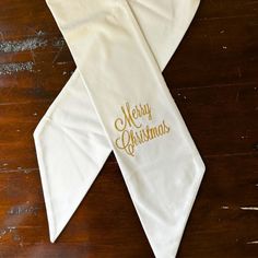 a white scarf with merry christmas written on it sitting on top of a wooden table