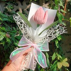 a hand holding up a pink flower with lace on it