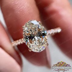 a close up view of a person's hand holding an oval shaped diamond ring