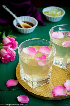 two glasses filled with liquid sitting on top of a wooden tray next to pink flowers