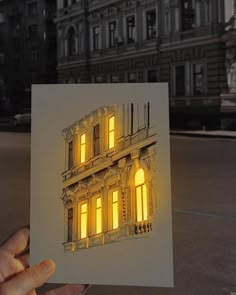 a hand holding up a card with an image of a building lit up at night