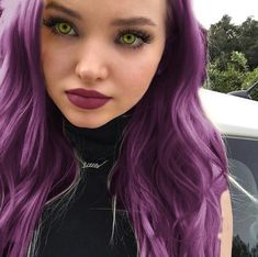 a woman with long purple hair and green eyes is posing for a photo in front of a car