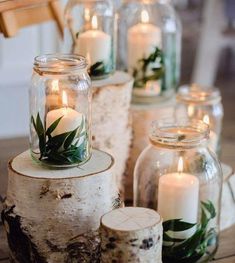 candles are lit in glass jars with greenery on them, along with birch logs