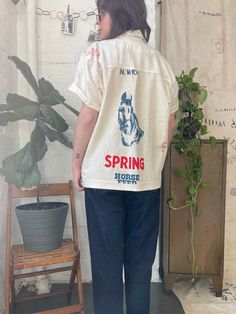 a woman standing in front of a potted plant wearing a white shirt with the words spring on it