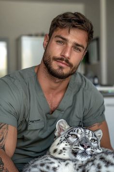 a man in grey shirt holding a white and black snow leopard laying on his chest