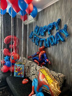 balloons and streamers are hanging from the ceiling in front of a couch with spiderman decorations