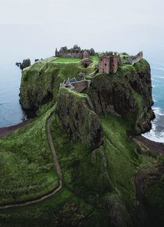 an old castle sits on top of a cliff by the ocean, surrounded by lush green grass