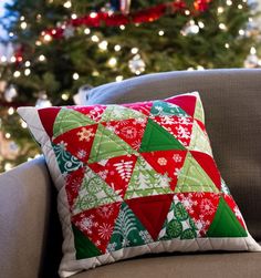 a red and green pillow sitting on top of a couch next to a christmas tree