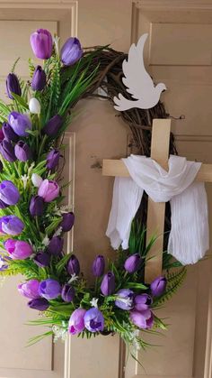 a wreath with purple and white flowers hanging on the front door next to a cross