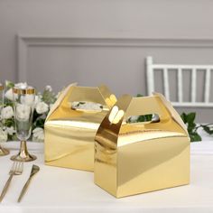 two gold boxes sitting on top of a table next to silverware and white flowers