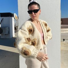 a woman standing next to a white wall wearing a sweater with teddy bears on it