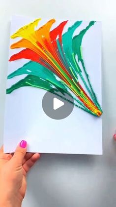 someone holding up a piece of paper with colorful paint on it and the video below