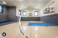 an indoor basketball court with hard wood flooring and climbing wall in the back ground