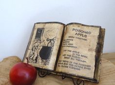 an open book sitting on top of a wooden table next to an apple and metal stand