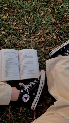 an open book sitting on top of a pair of white shoes next to someone's legs